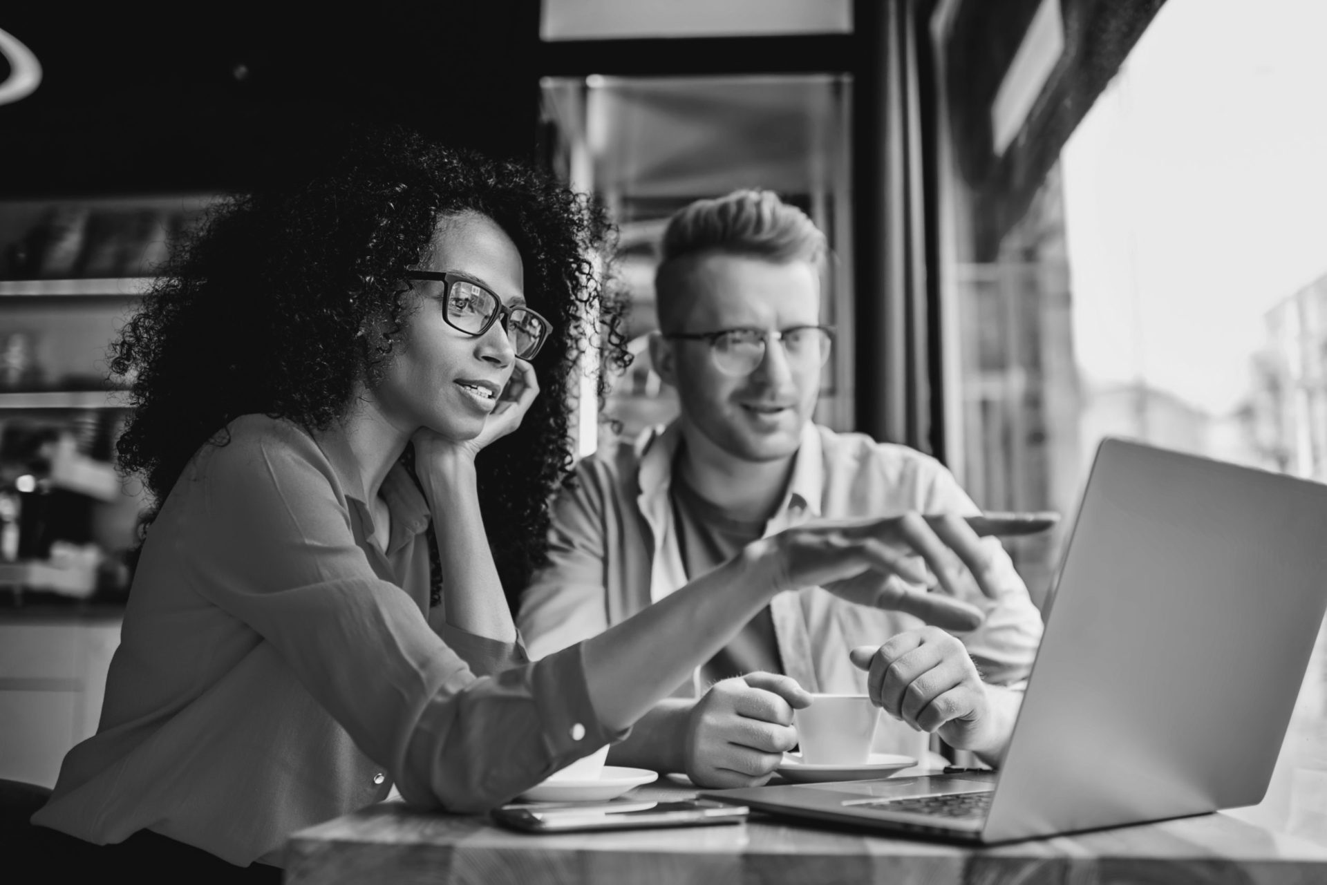 Dark skinned female graphic designer pointing with finger on laptop computer during collaboration with caucasian colleague on common project in coffee shop.Two multicultural friends discussing website